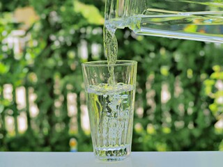 closeup Drinking water is pour from a jug in green garden blurred background