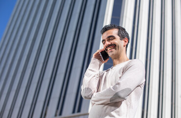 Joven trabajador ejecutivo feliz hablando por el teléfono móvil en el descanso del trabajo con oficinas a su espalda