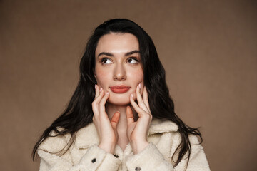 Photo of young woman in jacket touching her face and looking upward