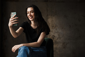 Photo of beautiful smiling woman sitting on chair and holding cellphone