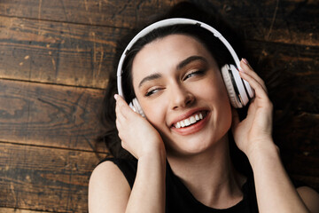 Photo of young woman wearing headphones smiling and lying on floor