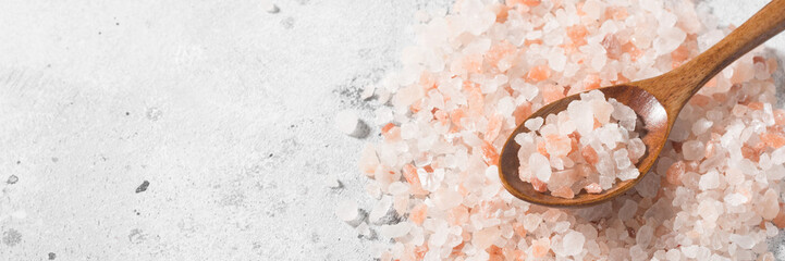 Fototapeta na wymiar Pink salt in a wooden spoon on a light gray table. Salt in a spoon and on the table. Pink sea salt close-up. Banner with space for text