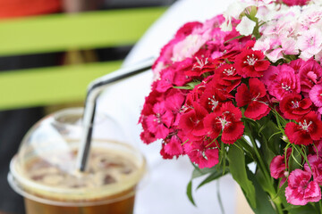 A bouquet of Chinese carnations on a table in a street cafe. Defocused, refreshing, coffee cocktail with ice in the background. Copy space - summer concept, flowers, walk, drinks, warm