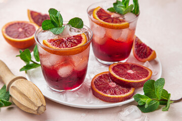 red blood orange cocktail with ice and fresh mint, top view, pink  background