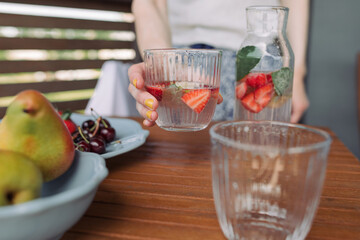 Woman holding glass of cool drink with fresh berries and lemon. Home summer picnic.