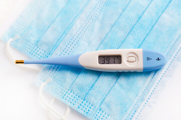 Close up of electronic thermometer and medical mask indicating high fever
