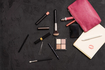 Overhead view of make up products spilling out of a pink cosmetics bag on a black background