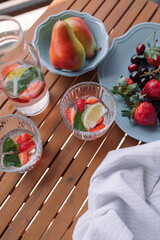 Top view of a glass with cool lemonade made of berries, lemon and mint leaves on wooden table at summer terrace. 