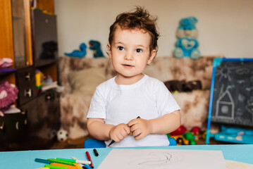 a small boy draws on sheets of paper lying on the table with colored pencils