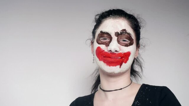 Portrait of girl with joker make up dances then smiles and waves hand. White background