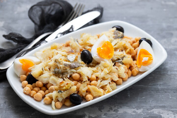 chick peas with cod fish, olives and boiled egg in white dish on ceramic background