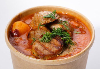 Ukrainian national cuisine - red borsch with vegetables, meat and dill. Sour soup in a paper cup on a white background.