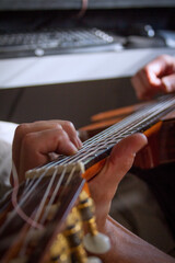 Vertical close up of man's hand playing flamenco guitar with computer in the background.