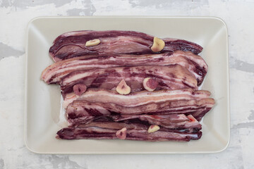 raw meat marinated in wine and garlic on grey dish on ceramic background