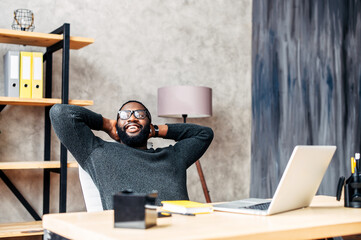 Take a break on a workplace. A young African-American guy leaned back in his chair relaxed, he is pleased with the work done