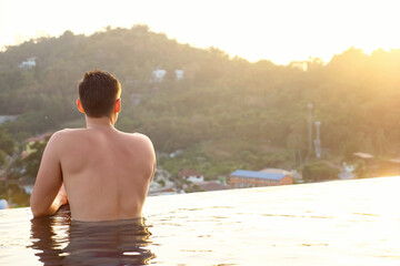 man in hotel outdoor swimming pool looking at pictorial tropical forestry hilly landscape backside view