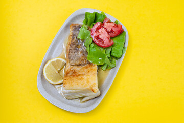 fried cod fish with fresh salad on dish on yellow background