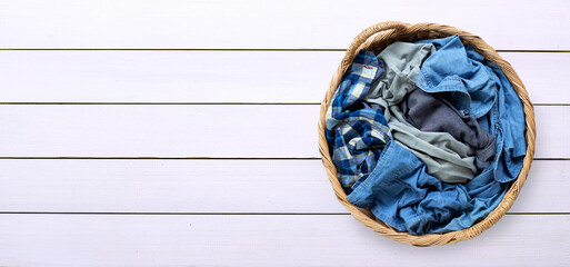 Clothes in laundry basket on white wooden background.