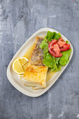 fried cod fish with fresh salad on dish on ceramic background