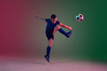 Fototapeta na wymiar Teen male football or soccer player on gradient background in neon light. Caucasian expressive boy training, practicing on the run, in jump. Concept of sport, competition, winning, motion, action.