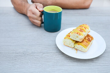 Cheese bread in a plate and cropped hand holding a mug of coffee on wooden table 