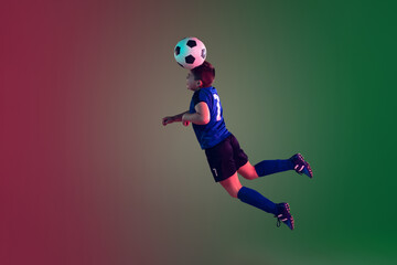 Fototapeta na wymiar Teen male football or soccer player on gradient background in neon light. Caucasian expressive boy training, practicing on the run, in jump. Concept of sport, competition, winning, motion, action.