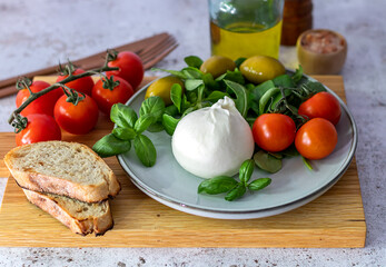 Fresh Italian burrata cheese with tomato on a light plate with basil and olives. Close up. Selective focus