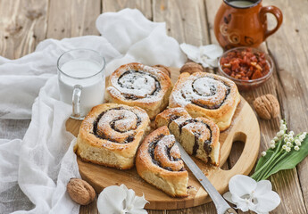 Basket of homemade buns with jam, served on old wooden table with walnuts and cup of milk