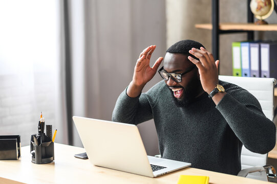 Overjoyed African Man Raised Hands Up, A Guy In Glasses Excited And Happy With A Good News Or Deal, He Looks At Laptop Screen With Triumph