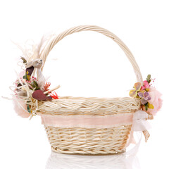 Fototapeta na wymiar Wicker basket of natural vines with floral decor and ribbons on white background. The basket decor is made in delicate pink tones for Easter celebration.