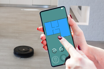 Close-up Of A woman Holding Remote Control Of Robotic Vacuum Cleaner To Start Cleaning