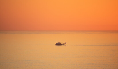 Naklejka premium Fishing boat sailing across Camps Bay in golden orange sunset light.