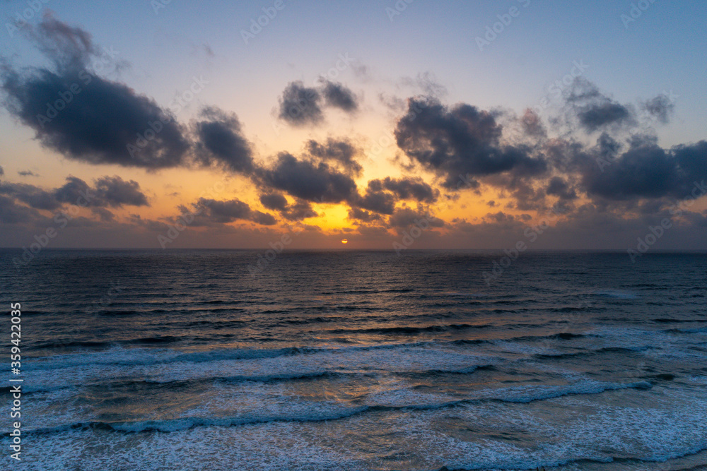 Wall mural beautiful sunset with dark blue sky and orange golden colors sun over the sea with dramatic clouds i