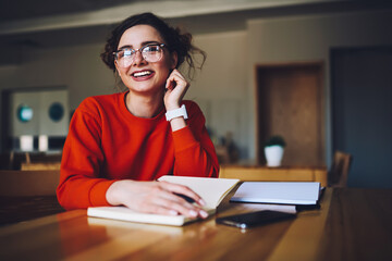 Portrait of cheerful funny hipster girl learning in university library writing report in copybook, smiling female student satisfied with getting good mark for coursework doing home task in campus