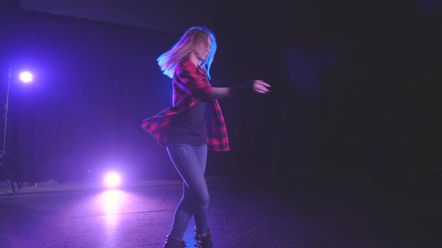 Beautiful woman professionally spinning on rollerblades on front wheels with crossed legs on dark platform under lighting of blue and pink spotlights in slow motion. Casting and performance from girl.