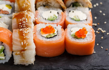 Two types of sushi with salmon and tuna, avocado and cucumber, cheese, sesame and caviar on a black stone sushi board.