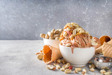 Peanut butter ice cream. Sweet peanut ice cream with peanut butter topping and a lot of peanuts, on grey stone background with icecream waffle cones