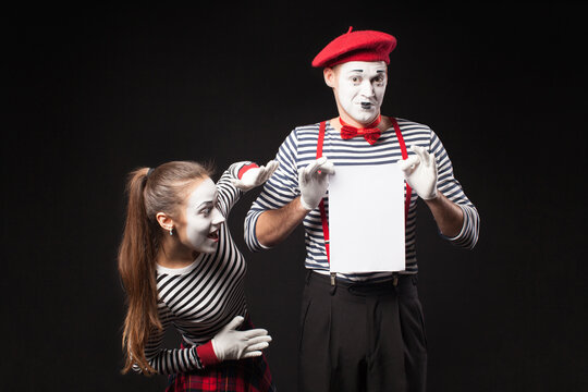 Two mimes man and woman  present white paper on isolated black background