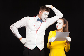 man and woman with white makeup on their faces like mimes present a blank white sheet of paper on a...
