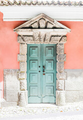 A turquoise blue old textured door, front view of a pink building
