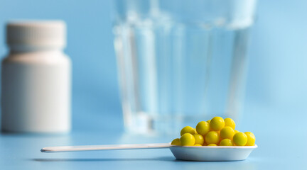Vitamin or pharmaceutical pills in a white spoon on the background of a glass glass with water and a white medicine bottle. Food additive, medical product, health concept