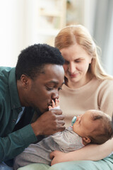 Vertical portrait of young interracial couple focus on African-American man kissing tiny hand of mixed-race baby