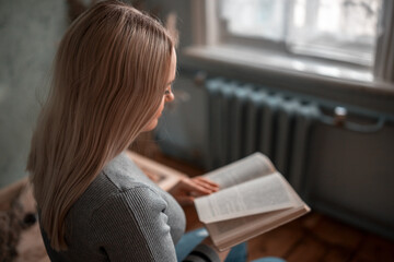 The girl is sitting at the table and reading a book