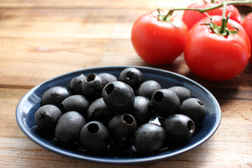 Bowl of black olives and fresh tomatoes on the vine on rustic wooden table background. Pasta or salad ingredients. Top view, copy space. 

