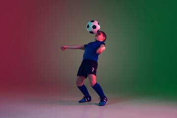 Fototapeta na wymiar Unstoppable. Teen male football or soccer player on gradient background in neon light. Caucasian boy training, practicing on the run, in jump. Concept of sport, competition, winning, motion, action.