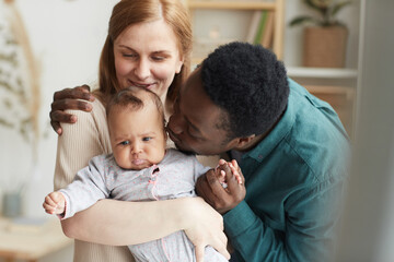 Waist up portrait of loving interracial family at home, focus on African-American man kissing cute mixed race baby - obrazy, fototapety, plakaty