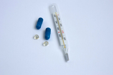 Blue pills, medicines in capsules and a thermometer on a white background