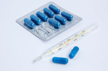 Blue pills, medicines in capsules and a thermometer on a white background