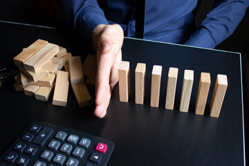 Male hand prevents wooden blocks from falling on the office desk. In the frame is a calculator, pen...