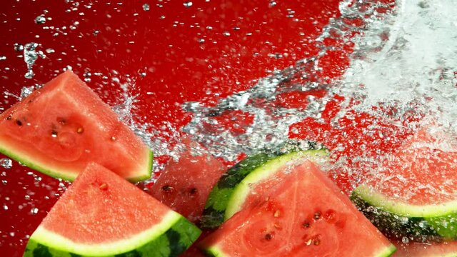 Super slow motion of water melon pieces flying up in the air with water splashes